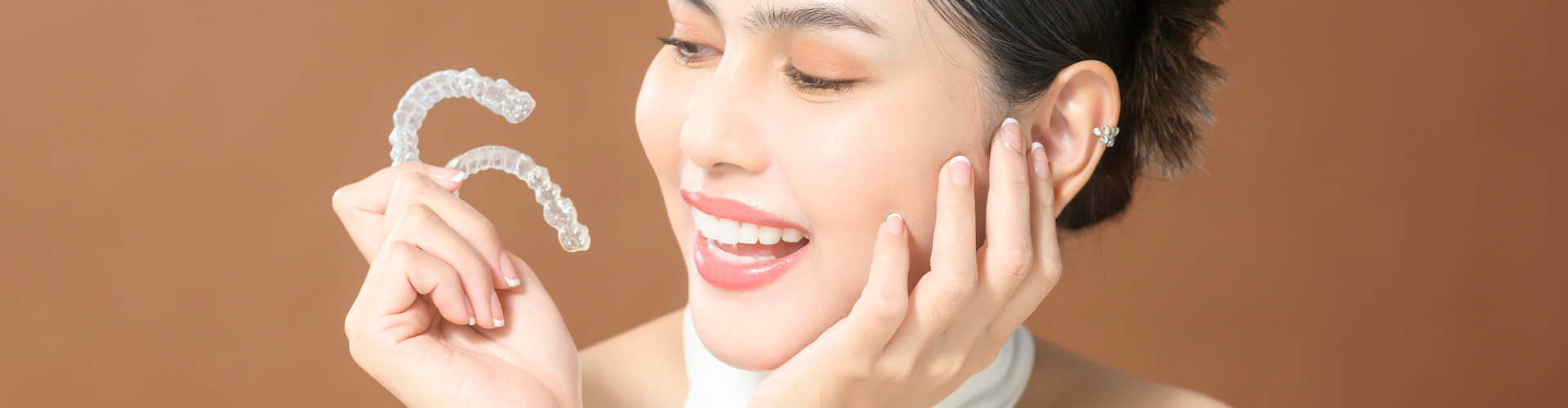 Smiling woman holding clear aligners in her hand.